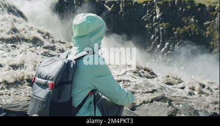 Femme assise et appréciant le bord de la puissante cascade de Detifoss en Islande Banque D'Images