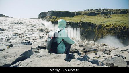 Femme assise au bord de la falaise en admirant la cascade de Detifoss en Islande Banque D'Images