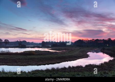 Le soleil levant baigne la rivière, les arbres, le ciel et les nuages dans une lumière rouge. Banque D'Images