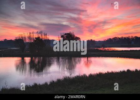 Le soleil levant baigne l'eau, les arbres, le ciel et les nuages dans une lumière rouge. Banque D'Images