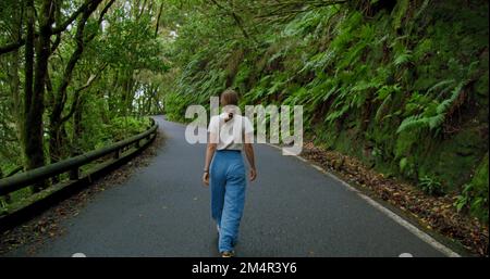 Une femme marche le long d'une route asphaltée dans une forêt dense. Arbres surcultivés dans la forêt d'arbres de Laurier ou la jungle, parc national d'Anaga, Tenerife, îles Canaries Banque D'Images