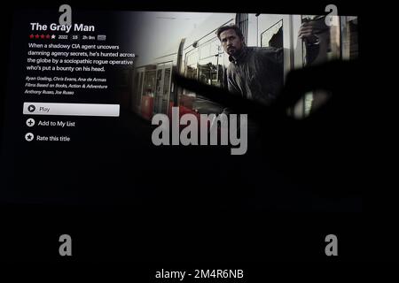 Application Netflix sur un écran de télévision mettant en évidence le film Netflix The Gray Man avec l'ombre d'une personne tenant une télécommande devant. Concept de superproduction à domicile. Banque D'Images