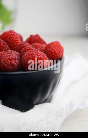gros plan de framboises fraîches dans un bol sombre, fond blanc flou Banque D'Images