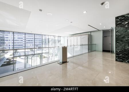 Atrium d'un immeuble de bureaux avec murs carrelés de marbre vert, sol en marbre crème, vue depuis une grande fenêtre mezzanine avec une rambarde en verre et un revolv Banque D'Images