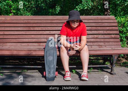 Garçon avec un skateboard en plastique assis sur la paillasse et fixe au téléphone. Banque D'Images