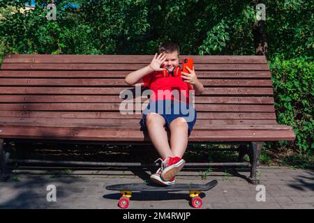 Garçon assis sur le banc et communique par chat vidéo à l'aide d'un smartphone et d'Internet. Banque D'Images