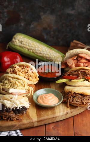 A closeup view of six differently flavored arepas served with sauce and a corn Banque D'Images
