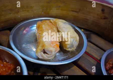 Le dimsum roulé est servi sur un bol en étain sur le bol vapeur en bois. Banque D'Images