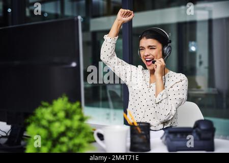 Oui, un autre client satisfait. une jeune femme d'affaires attirante applaudisse tout en travaillant tard dans un centre d'appels. Banque D'Images