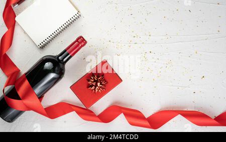 vue du dessus photo de la décoration de la st valentin avec boîte cadeau, bouteille de vin et ruban rouge en soie sur fond blanc isolé avec espace vide. Bannière Banque D'Images