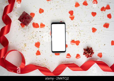 Smartphone avec écran isolé sur l'arrière-plan de la Saint-Valentin. Scène d'amour avec cadeau, coeurs et ruban. Maquette, espace de copie pour votre texte. Banque D'Images