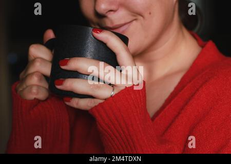 gros plan de la femme heureuse tenant une tasse de café grise, portant un pull doux et chaud rouge Banque D'Images
