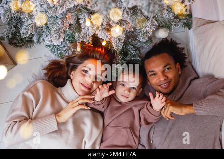 Une jeune famille heureuse avec un petit garçon est couché sur une couverture tricotée, sous un arbre de Noël. Banque D'Images