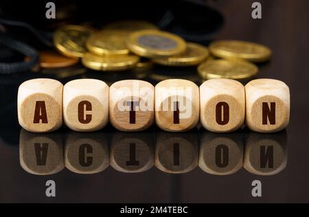 Concept d'affaires et d'économie. Sur une surface réfléchissante noire se trouvent des pièces de monnaie et des cubes de bois avec l'inscription - ACTION Banque D'Images