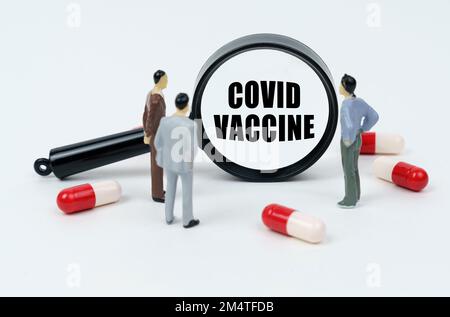 Concept médical. Sur une surface blanche sont des pilules, des figurines miniatures de personnes et une loupe avec l'inscription - COVID VACCIN Banque D'Images