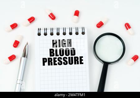 Concept médical. Sur une surface blanche se trouvent des comprimés, un stylo, une loupe et un bloc-notes avec l'inscription - hypertension Banque D'Images
