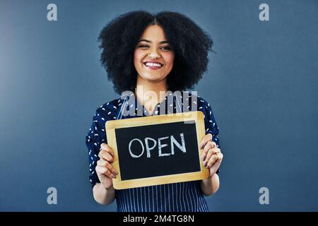 Bienvenue. client existant et nouveau Studio tourné d'une jeune femme tenant un tableau noir avec le mot ouvert sur lui sur un fond bleu. Banque D'Images