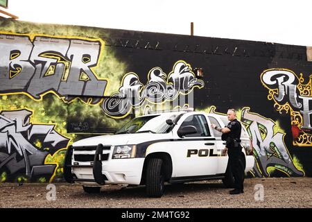 Image horizontale d'un policier blanc de race blanche sortant de sa voiture de cavalier dans sa ville avec des graffitis sur le mur comme toile de fond. Banque D'Images