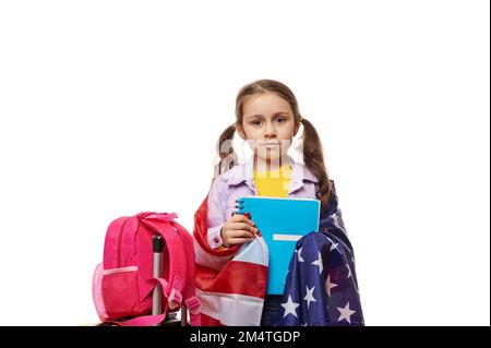 Fille intelligente avec deux queues de cheval, enveloppant dans le drapeau U.S.A, tenant le livre d'or dans ses mains, regardant avec confiance l'appareil photo Banque D'Images