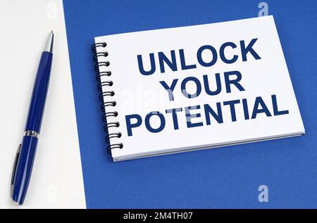 Concept commercial et financier. Sur une surface bleu-blanc se trouve un stylo et un bloc-notes avec l'inscription - Unlock Your Potential Banque D'Images
