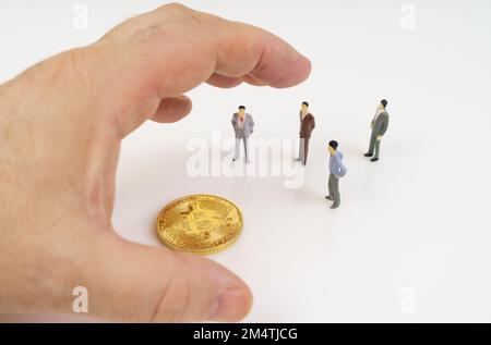 Crypto-monnaie et concept d'entreprise. Sur une surface blanche, bitcoin, figurines miniatures de personnes et une main humaine qui atteint pour bitcoin. Banque D'Images