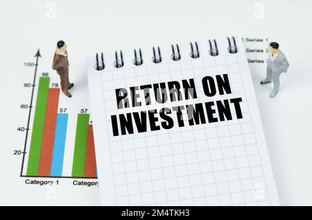 Concept commercial et financier. Sur la carte il y a des figures miniatures d'hommes d'affaires et un bloc-notes avec l'inscription - RETOUR SUR INVESTISSEMENT Banque D'Images