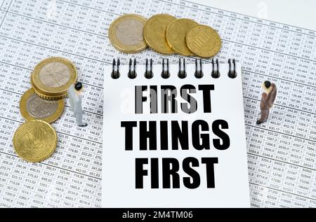 Concept commercial et financier. Sur les rapports financiers il y a des figurines de personnes, des pièces et un bloc-notes avec l'inscription - First Things First Banque D'Images