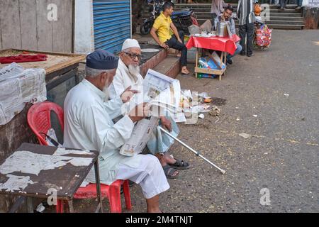 Deux musulmans âgés assis à l'extérieur de la gare de Byculla à Mumbai, en Inde, dont un lisant un journal en ourdou Banque D'Images