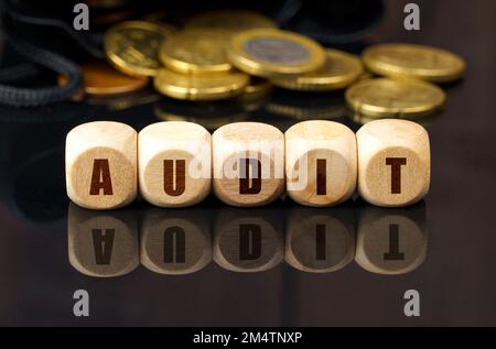 Concept d'affaires et d'économie. Sur une surface réfléchissante noire se trouvent les pièces de monnaie et les cubes de bois avec l'inscription - AUDIT Banque D'Images