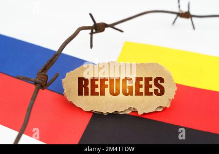 Concept politique. Sur les drapeaux de l'Allemagne et de la Russie se trouve une plaque de carton avec l'inscription - réfugiés. Drapeaux séparés par un fil barbelé Banque D'Images