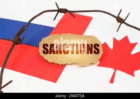 Concept politique. Sur les drapeaux du Canada et de la Russie se trouve une plaque de carton avec l'inscription - sanctions. Drapeaux séparés par un fil barbelé Banque D'Images