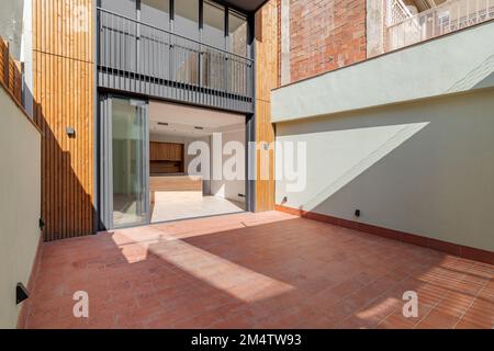 Bâtiment résidentiel sur plusieurs étages avec portes coulissantes en métal noir et verre. La porte s'ouvre sur une cuisine dotée de meubles en bois clair. Patio Banque D'Images