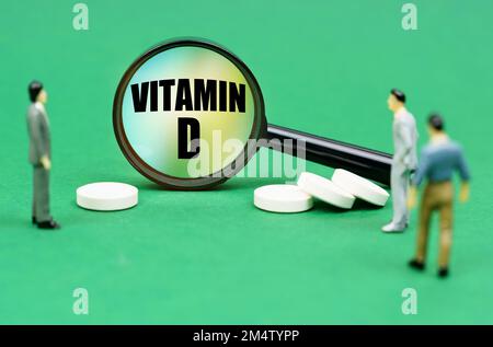 Concept médical. Sur une surface verte sont des pilules, des figures miniatures de personnes et une loupe avec l'inscription - vitamine D. Banque D'Images