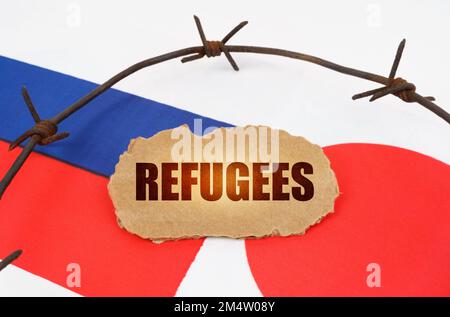 Concept politique. Sur les drapeaux du Japon et de la Russie se trouve une plaque de carton avec l'inscription - réfugiés. Drapeaux séparés par un fil barbelé Banque D'Images
