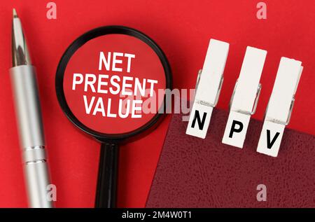 Business concept. On the red surface lies a pen, a notebook with clothespins - NPV, and a magnifying glass with the inscription - Net Present Value Banque D'Images