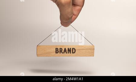 Mot de marque. Écrit sur un panneau en bois accroché à la main humaine Banque D'Images