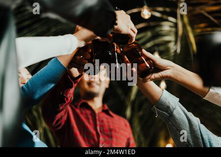 Groupe de gens asiatiques heureux amis célébrant et se clinquant avec des bouteilles de bière Banque D'Images