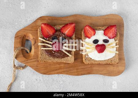 Deux toasts doux pour les enfants en forme de chat avec fraises, banane, fromage à la crème et chocolat sur bois, vue du dessus Banque D'Images