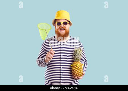 Joyeux drôle barbu homme chubby avec ananas et filet d'insecte sur fond bleu clair d'été. Banque D'Images