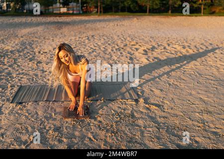 Vue avant de la jeune femme tenant le tableau Sadhu avec les ongles dans les mains et touchant les ongles pointus avec la paume sur la plage de sable à la journée ensoleillée d'été. Banque D'Images