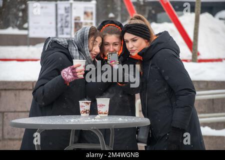 Trois belles filles en vêtements chauds buvant du vin chaud, souriant et prenant le selfie avec téléphone à la place de la cathédrale de Vilnius, Lituanie, Europe Banque D'Images