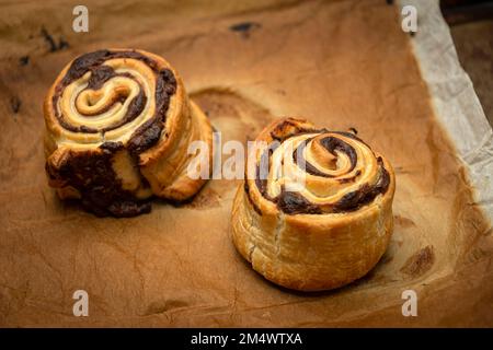 Des petits pains à la cannelle faits maison fraîchement cuits sortis du four sur une plaque de cuisson avec du papier brun. Banque D'Images