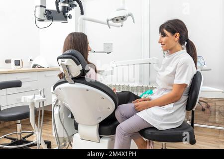 Dentiste féminin parlant à un jeune patient lors d'un rendez-vous dans une clinique dentaire moderne avant le traitement des dents Banque D'Images