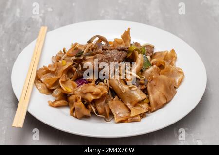 Nouilles frites avec légumes et bœuf dans un plat blanc sur rose Banque D'Images