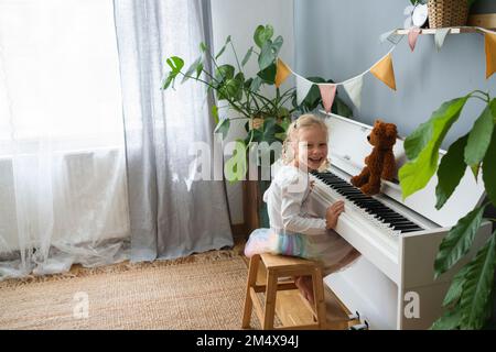 Bonne fille assise sur un tabouret au piano à la maison Banque D'Images