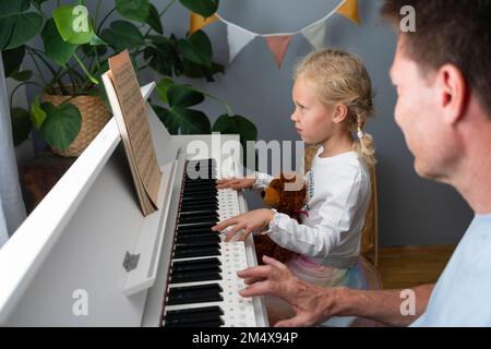 Fille lisant des notes musicales et jouant du piano à la maison Banque D'Images