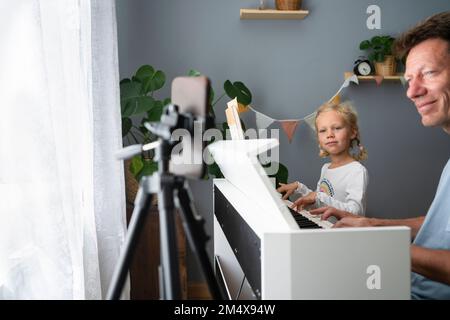 Père et fille apprenant à jouer du piano par téléphone portable à la maison Banque D'Images