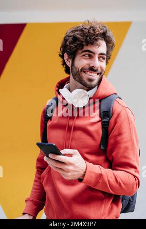 Heureux homme portant un sweat à capuche rouge devant un mur coloré Banque D'Images