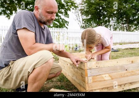 Père enseignant à la fille de mesurer le lit en bois levé dans la cour arrière Banque D'Images