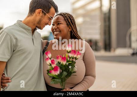 Joyeux jeune homme embrassant la femme debout avec un bouquet de fleurs Banque D'Images